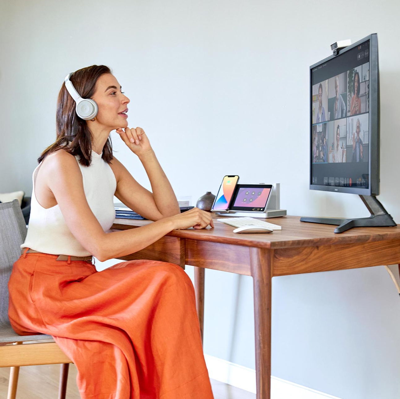 A person wearing headphones sits at a desk, watching a meeting on a computer monitor.  A Webex Desk Hub sits on the corner of the desk.