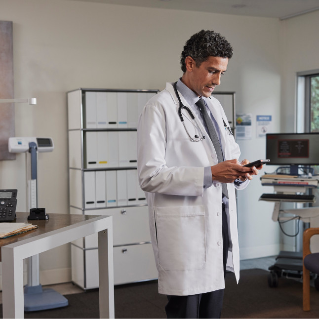 A doctor in a medical office looks at a mobile phone.