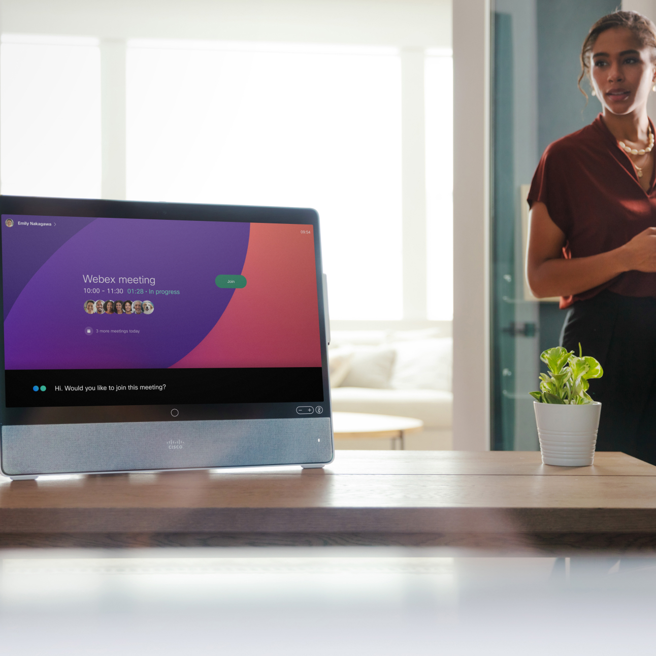 In the foreground, the Cisco Desk displays a meeting invitation. In the background, an employee approaches the desk.