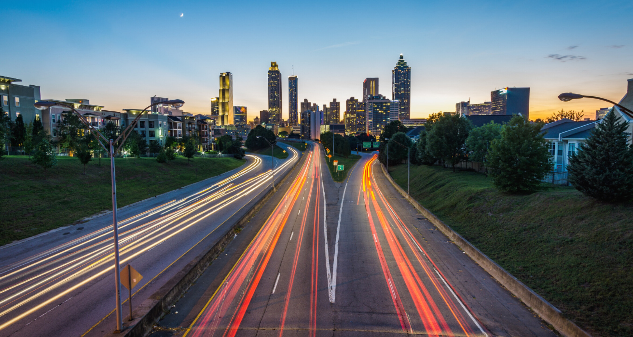 A cityscape at dusk. A multi-lane highway leading to a city with tall skyscrapers.