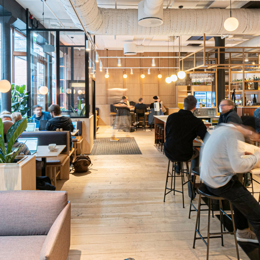 Several people work in a cafe-style workspace, with stools, booths, and tables.