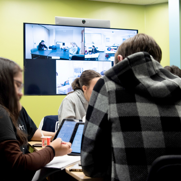 Children collaborate in person and remotely via Cisco Room Kit. Their teacher and classmates are visible on their screens.