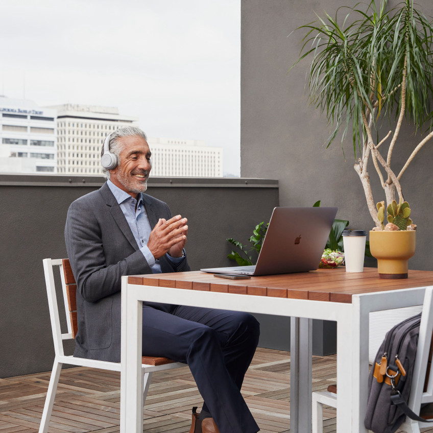 Person in a headset video conferences from his laptop in his office. Skyscrapers are seen outside  the window.